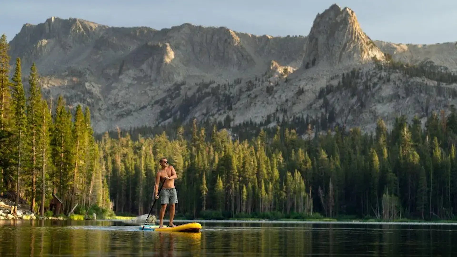 Person paddleboarding on calm alpine lake demonstrating full-body wellness workout and mental health benefits