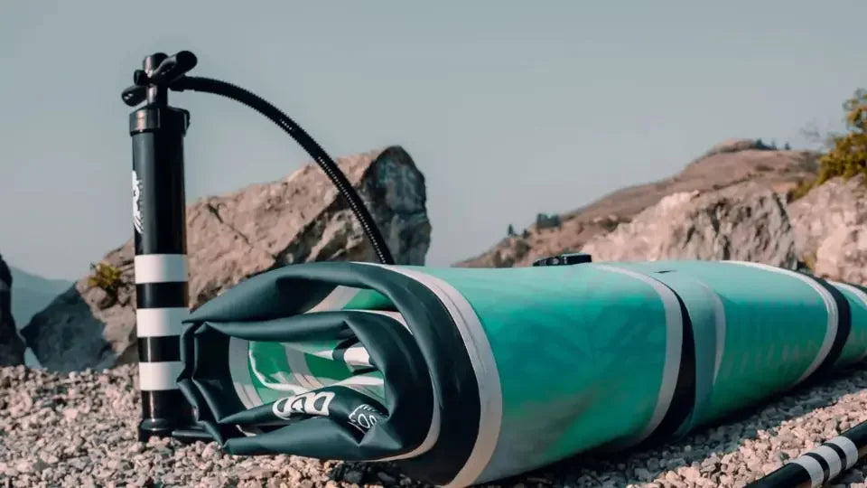 Folded inflatable paddle board with pump and paddle from POP Board Co on rocky shore