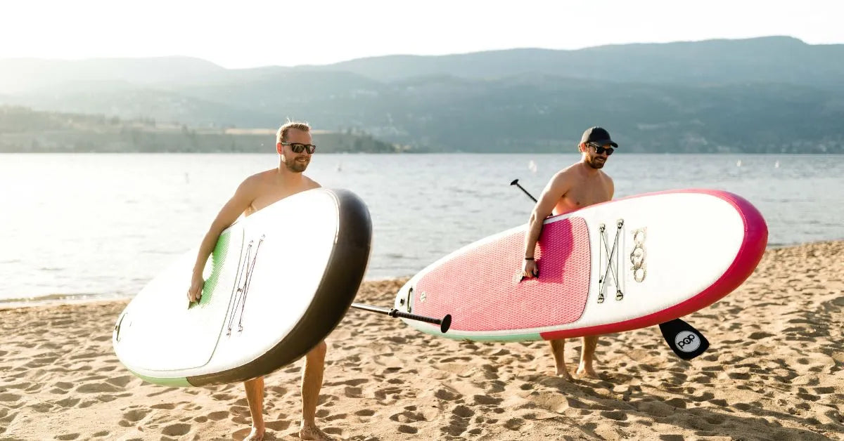 Men carrying inflatable paddle boards at lakeside beach in Canada