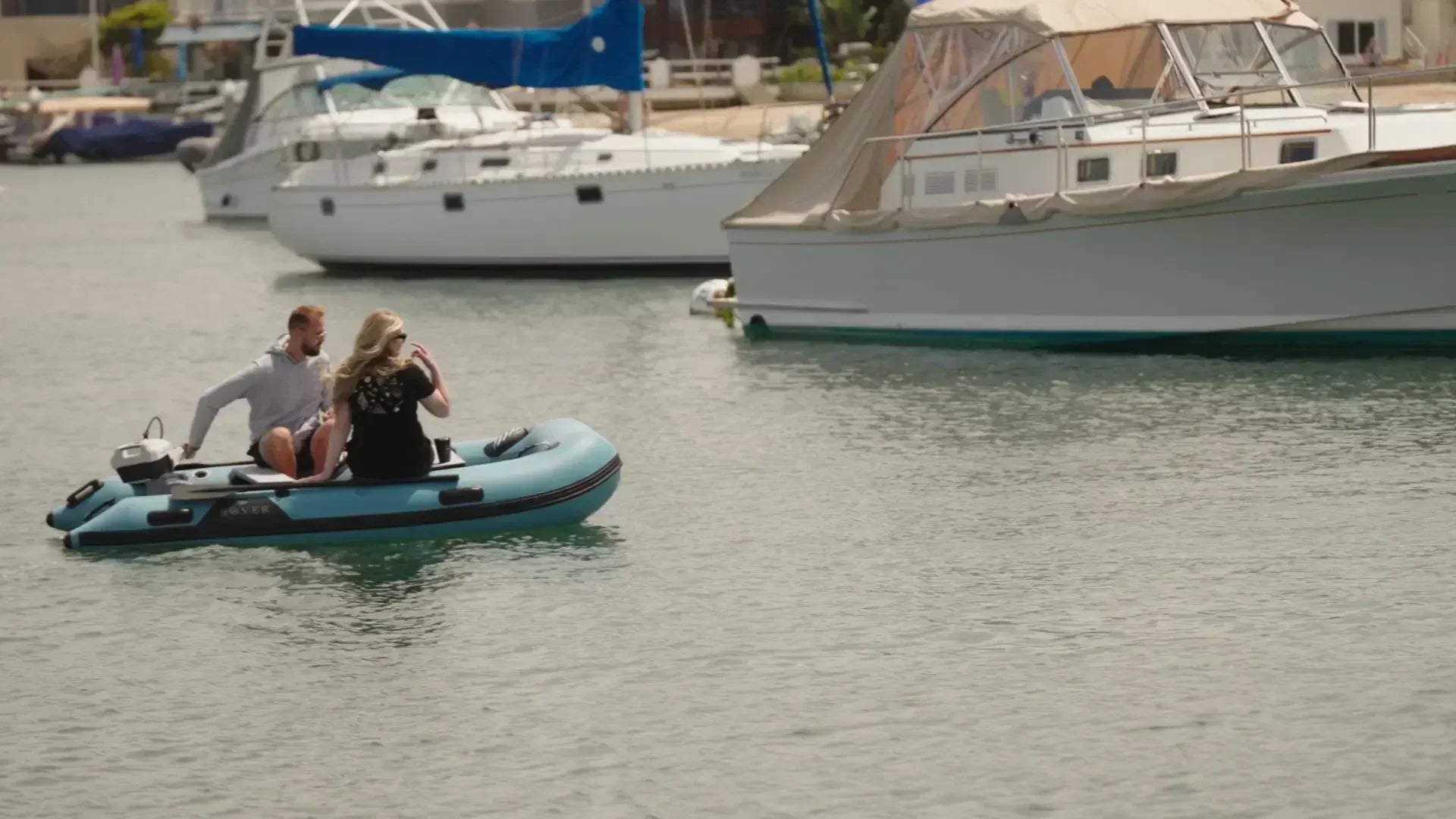 Two people cruising in a Rover Marine inflatable boat through a marina.