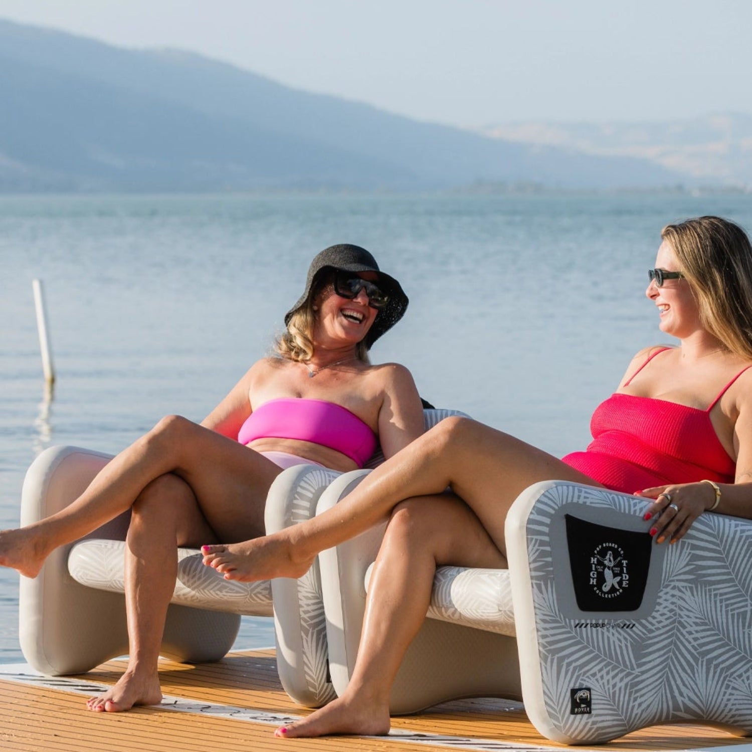 Two women sitting on a floating platform with a scenic lake background