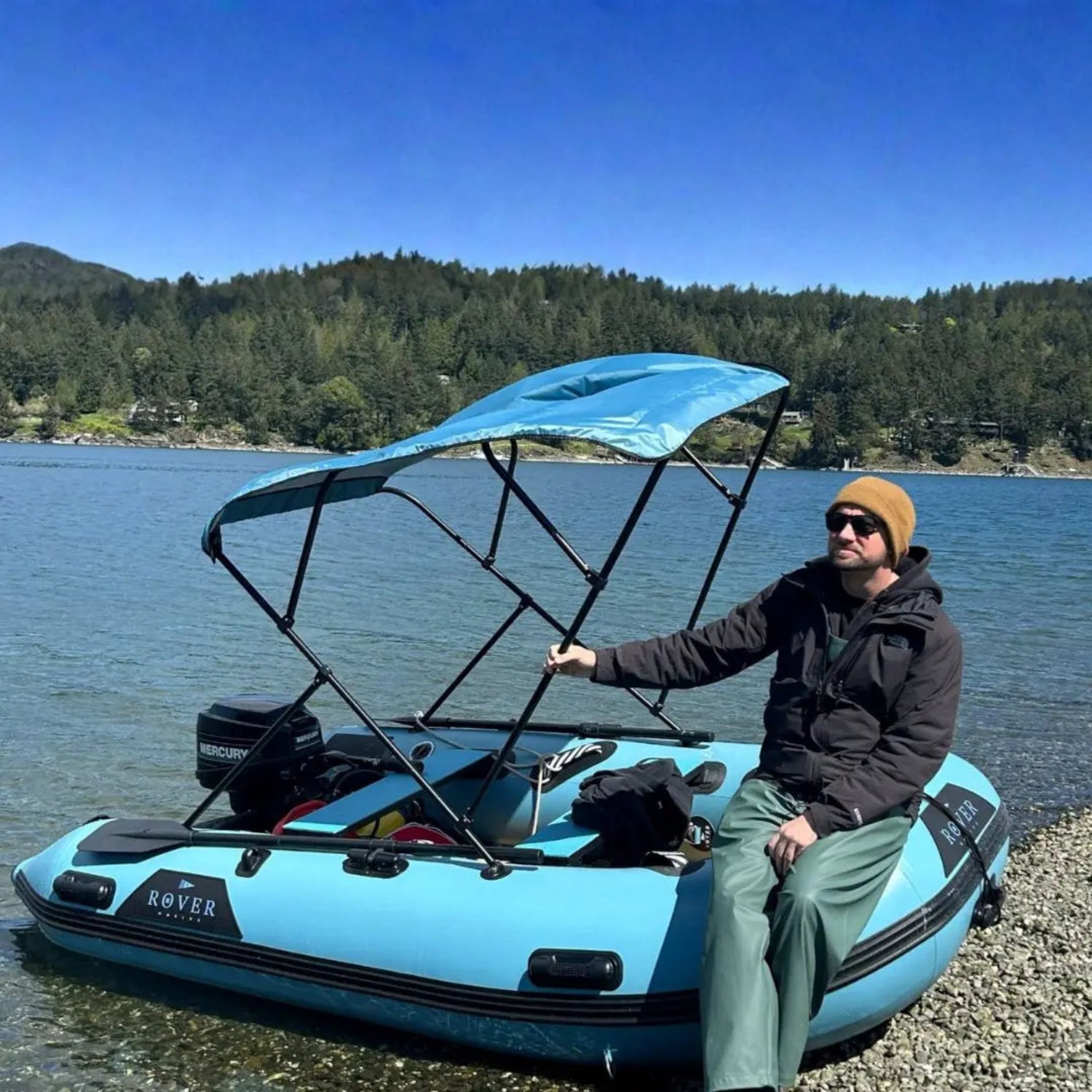 Man sitting on a blue inflatable boat with a canopy on a lake.