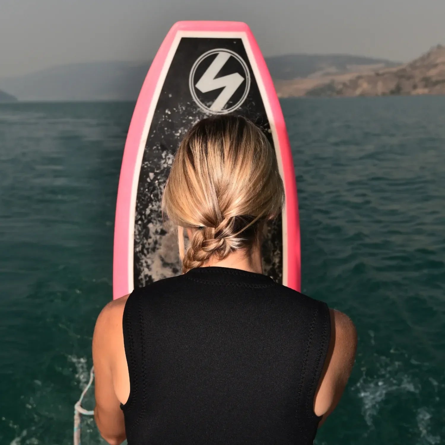 Woman holding Cassidy Pro Fuzzy Peach wakesurf board at the lake.