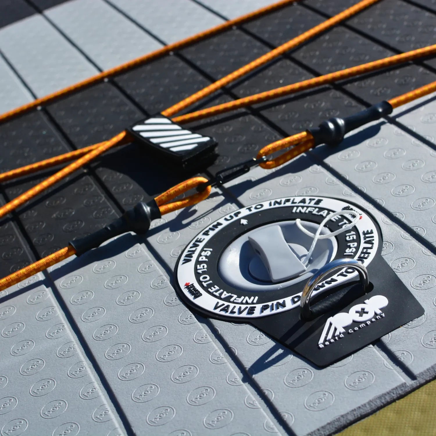 Close-up of the 11'6 El Capitan - Bomber paddleboard, highlighting its valve, orange ropes with black fittings, textured grey and black surface, handle, and POP logo—showcasing this stable board's quality design.
