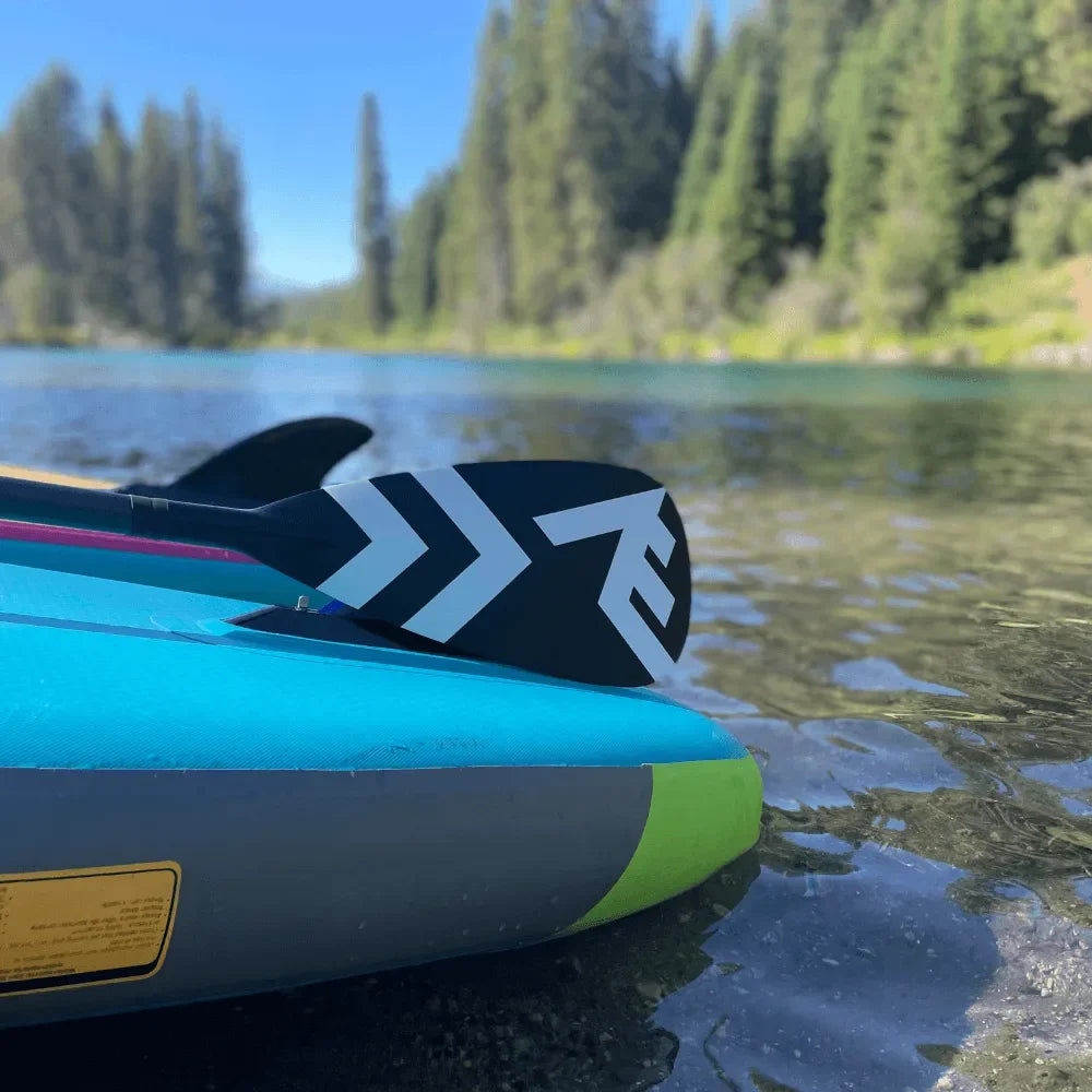 Close-up of inflatable paddle board with fin and paddle resting on clear lake water