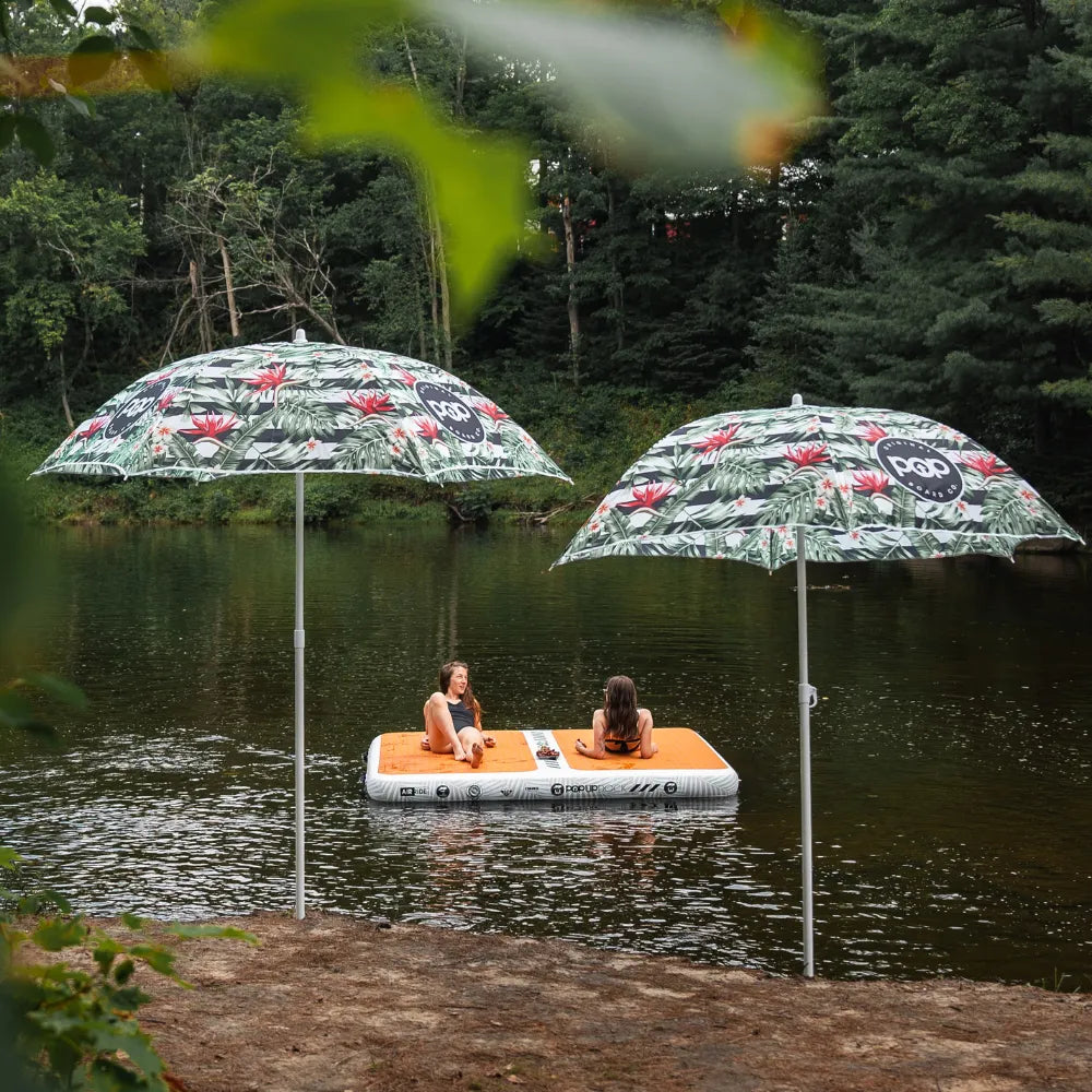 Two women relaxing on a POPUP Dock inflatable floating platform on a calm lake, surrounded by trees and nature.