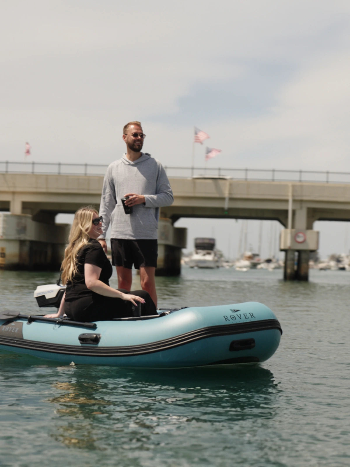 Couple enjoying a ride on Rover Marine inflatable boat on calm water near marina.