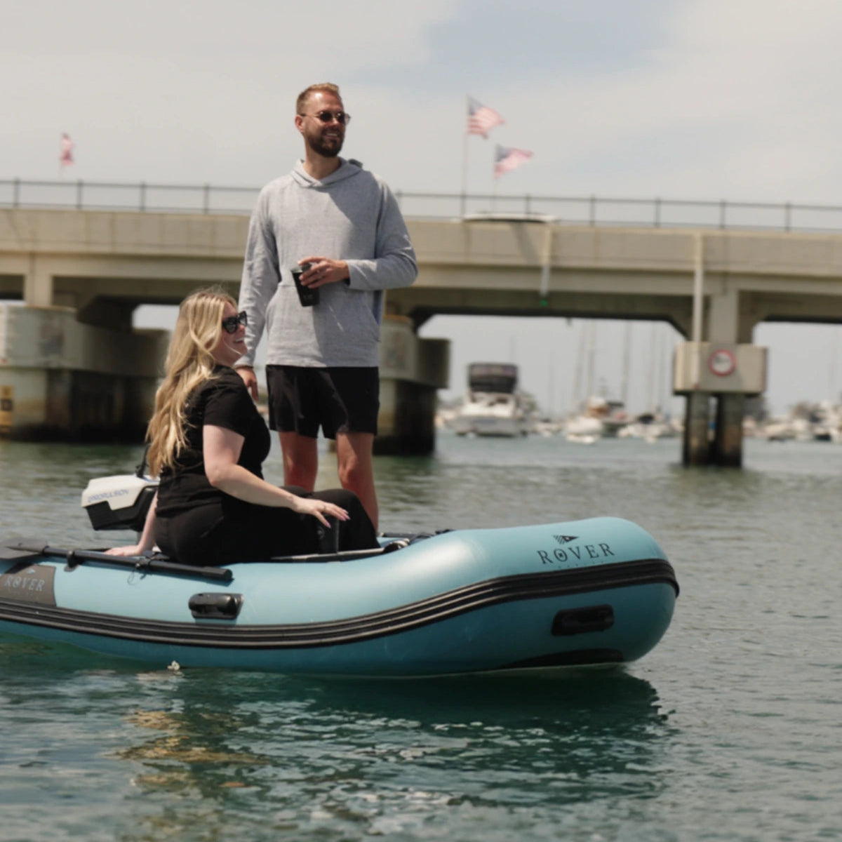 Couple enjoying a ride on Rover Marine inflatable boat on calm water near marina.