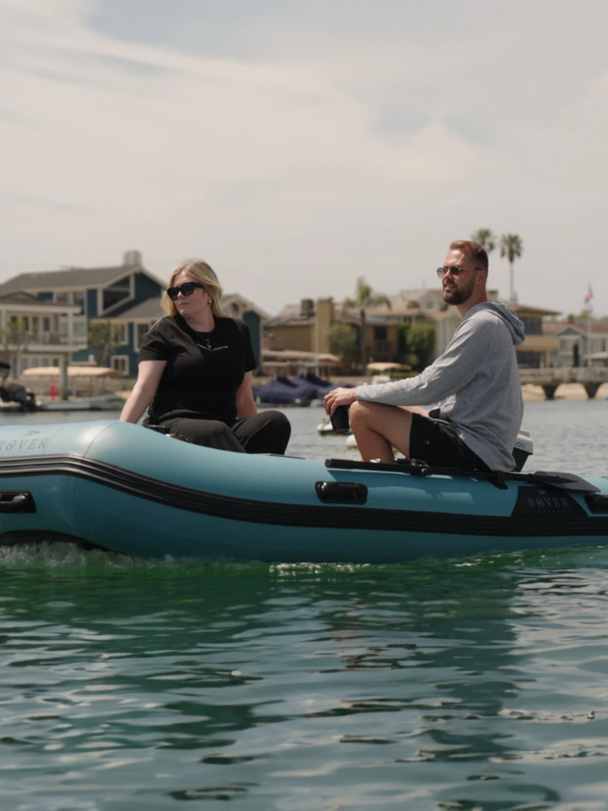 Man and woman relaxing on Rover Marine inflatable boat with waterfront homes in the background.