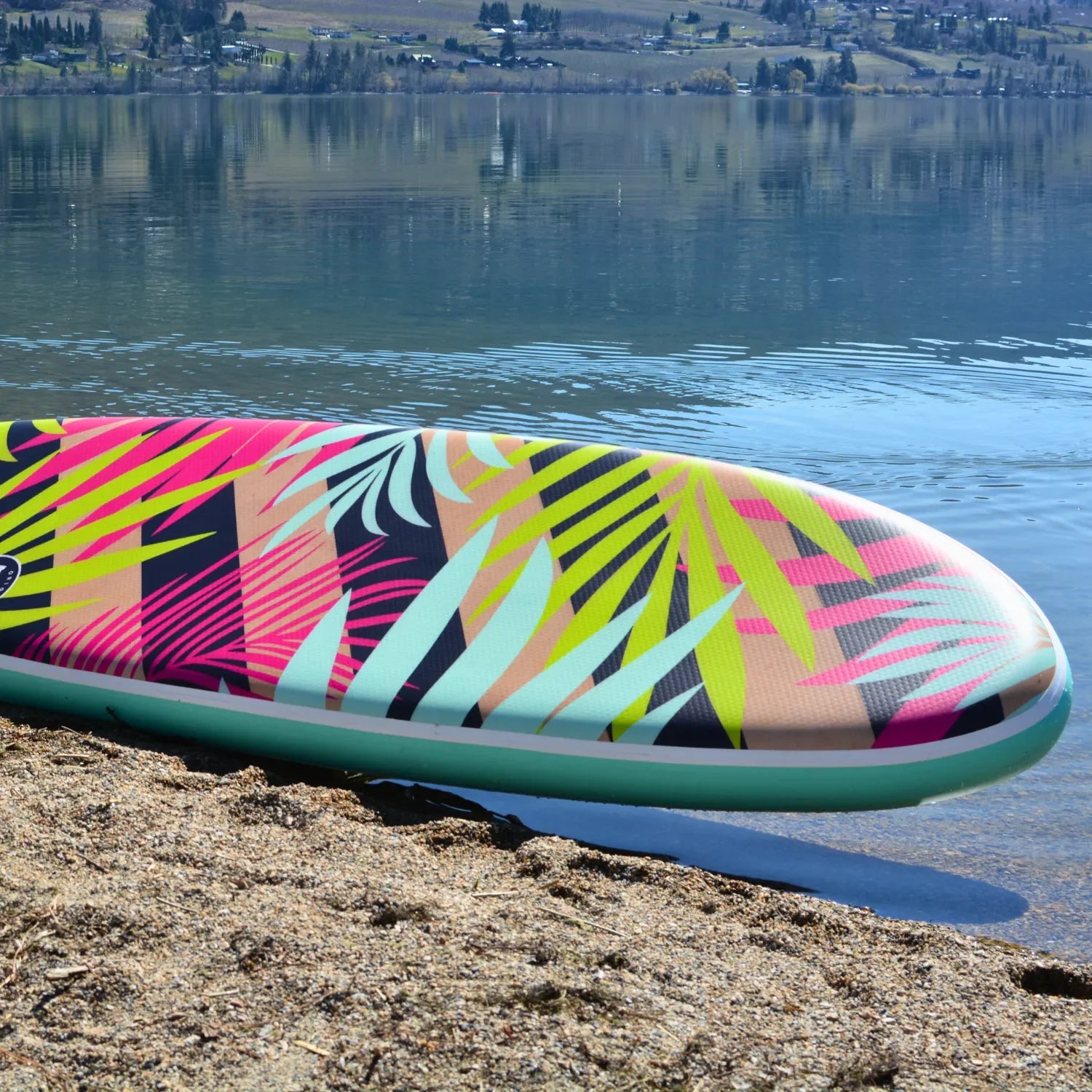 POP Royal Hawaiian 10’6 inflatable paddleboard resting at an angle on sandy lakeside beach.