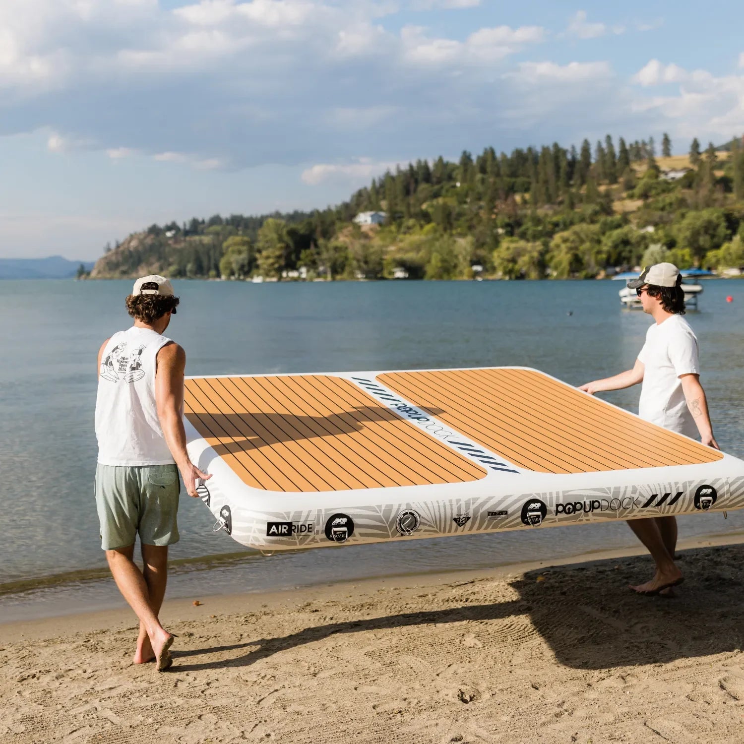 Two men carrying a POPUP Dock inflatable platform with wood-style traction pad from the beach into the water on a sunny day.