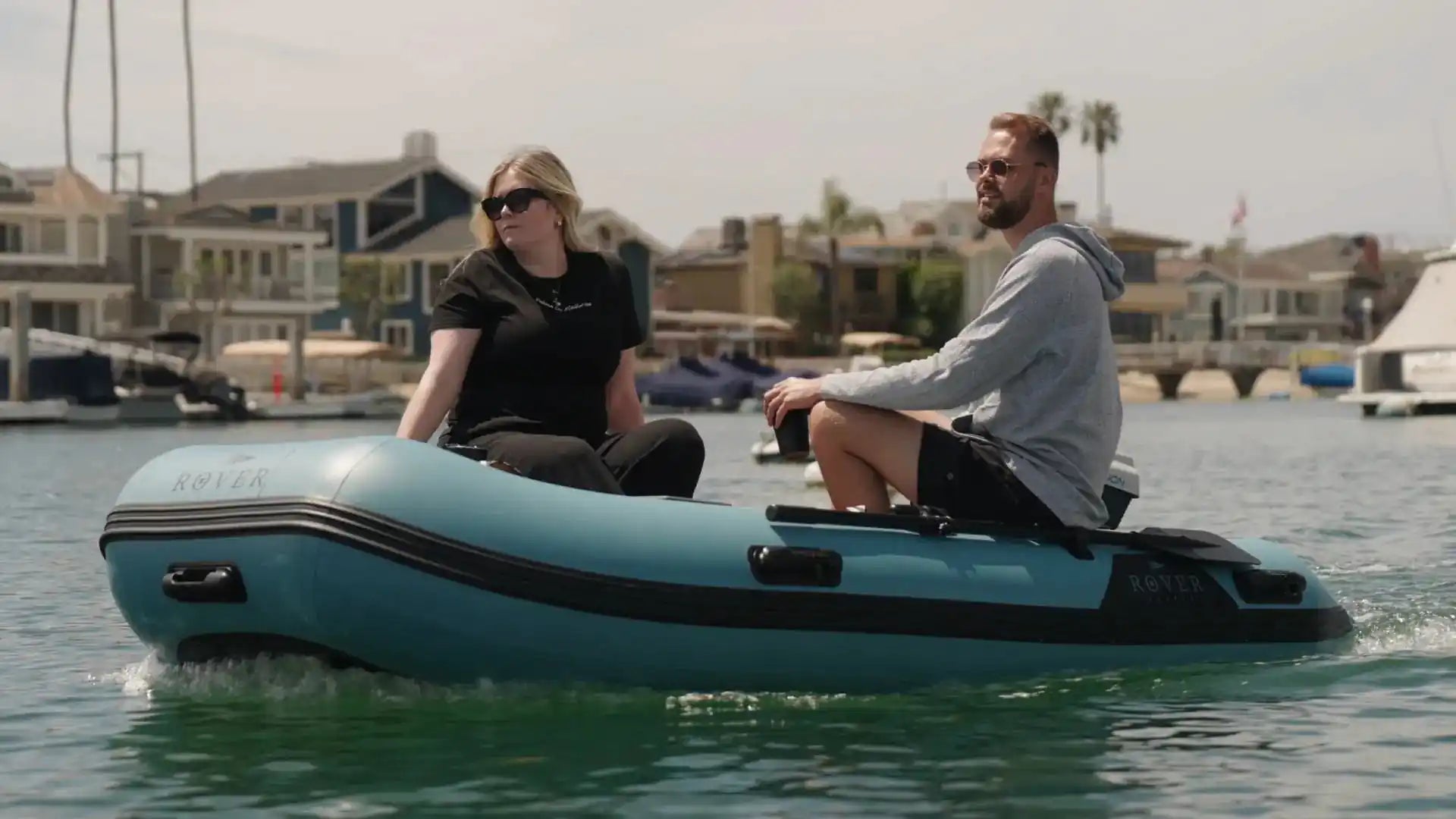 Two people on a small inflatable boat in a harbor.