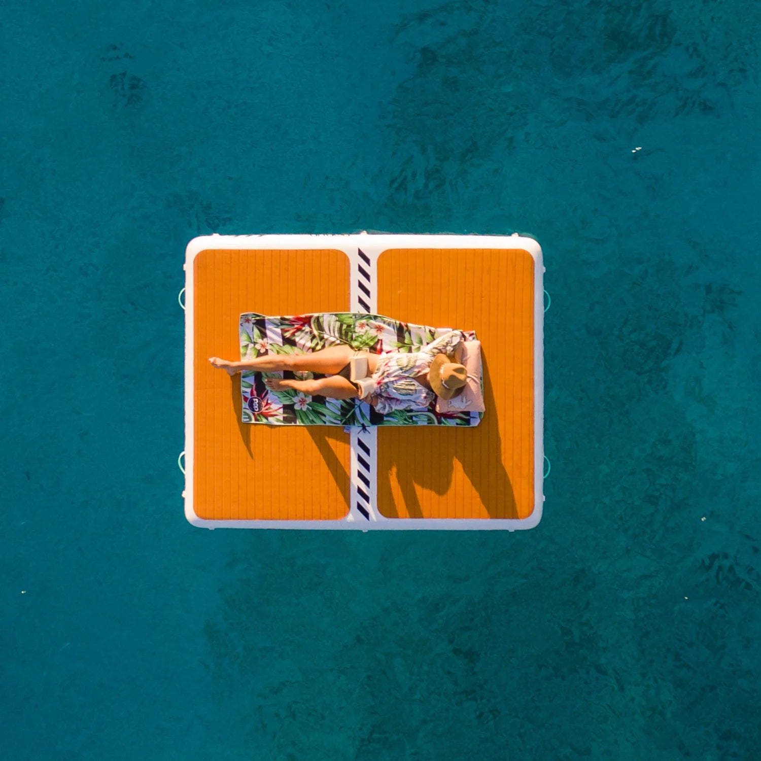 Aerial view of a used POP Up Dock with person lounging on top, floating on clear blue water.