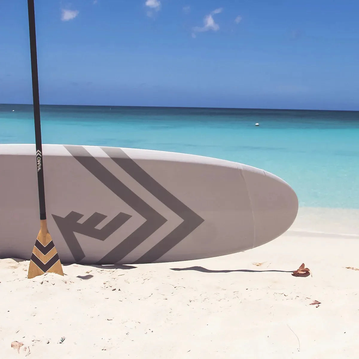 Bamboo Vamo SUP paddle resting on the sand with a paddleboard by the turquoise ocean, available at Canadian Board Co.