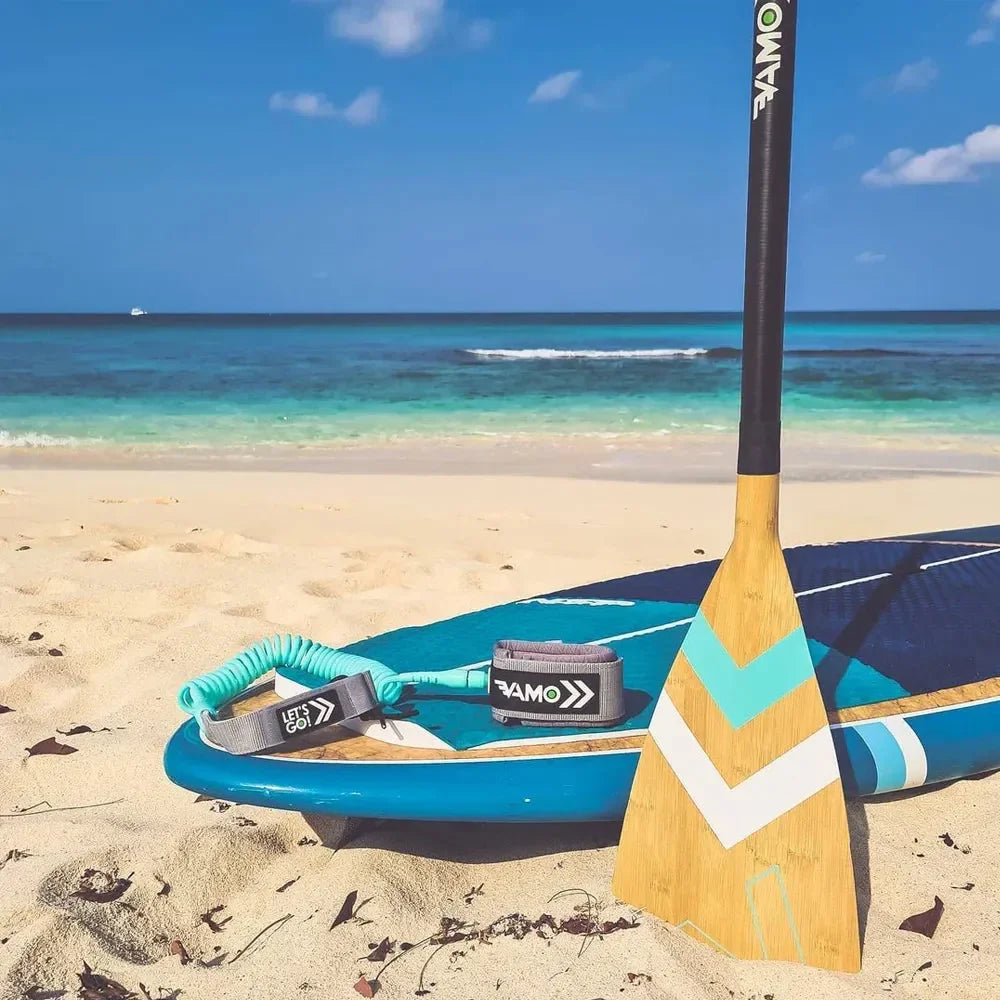 Bamboo Vamo SUP paddle with turquoise chevron design, standing next to a paddleboard on the beach.
