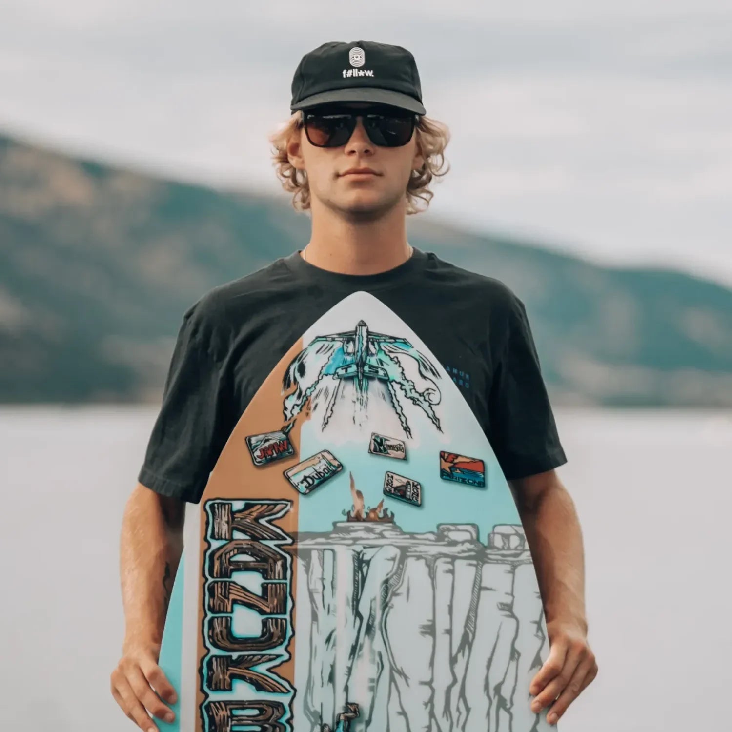 Rider holding Vedder Stewy Cliff Jump Pro wakeskim board near the lake.