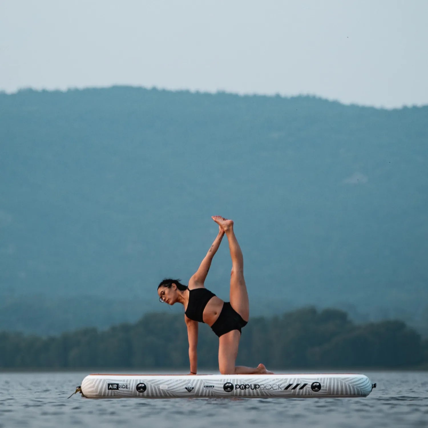 Woman performing yoga stretch pose on the POP inflatable dock, highlighting stability on water.