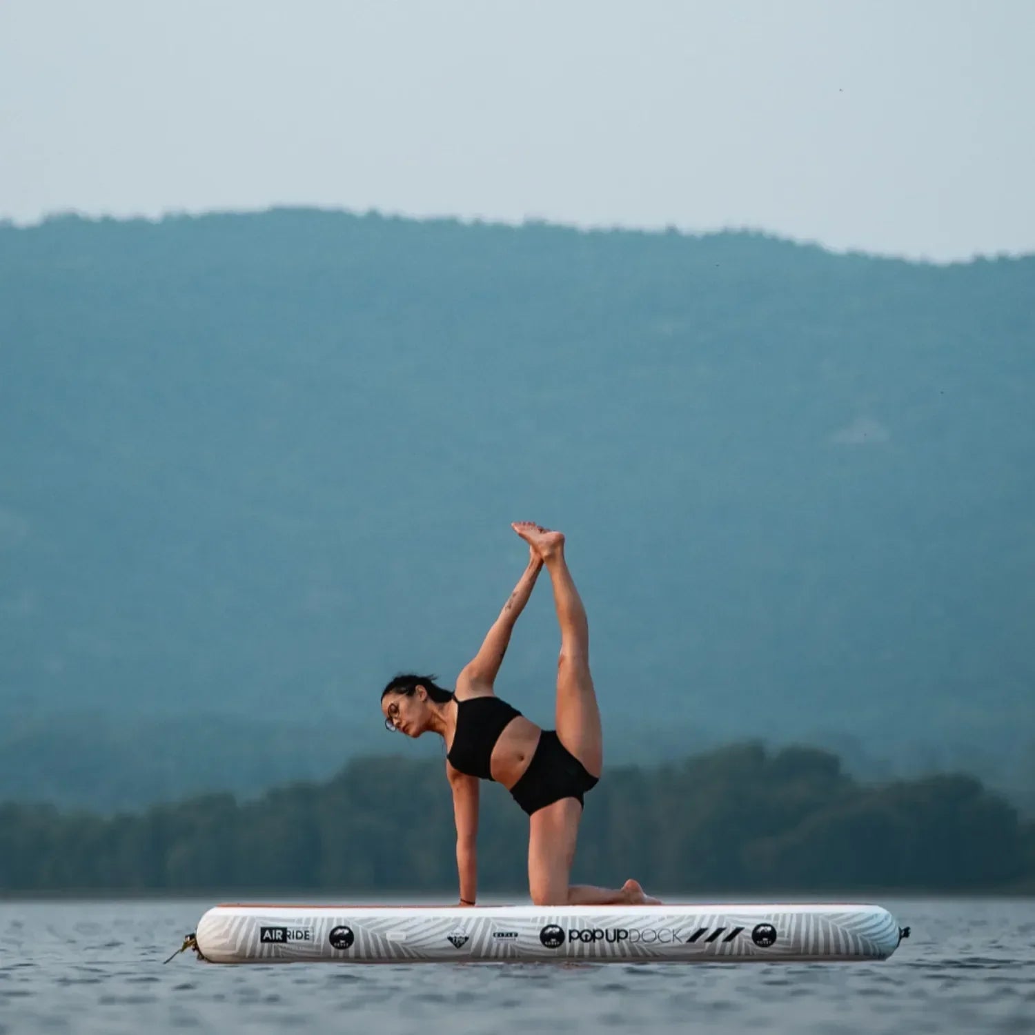 Woman performing yoga stretch pose on the POP inflatable dock, highlighting stability on water.