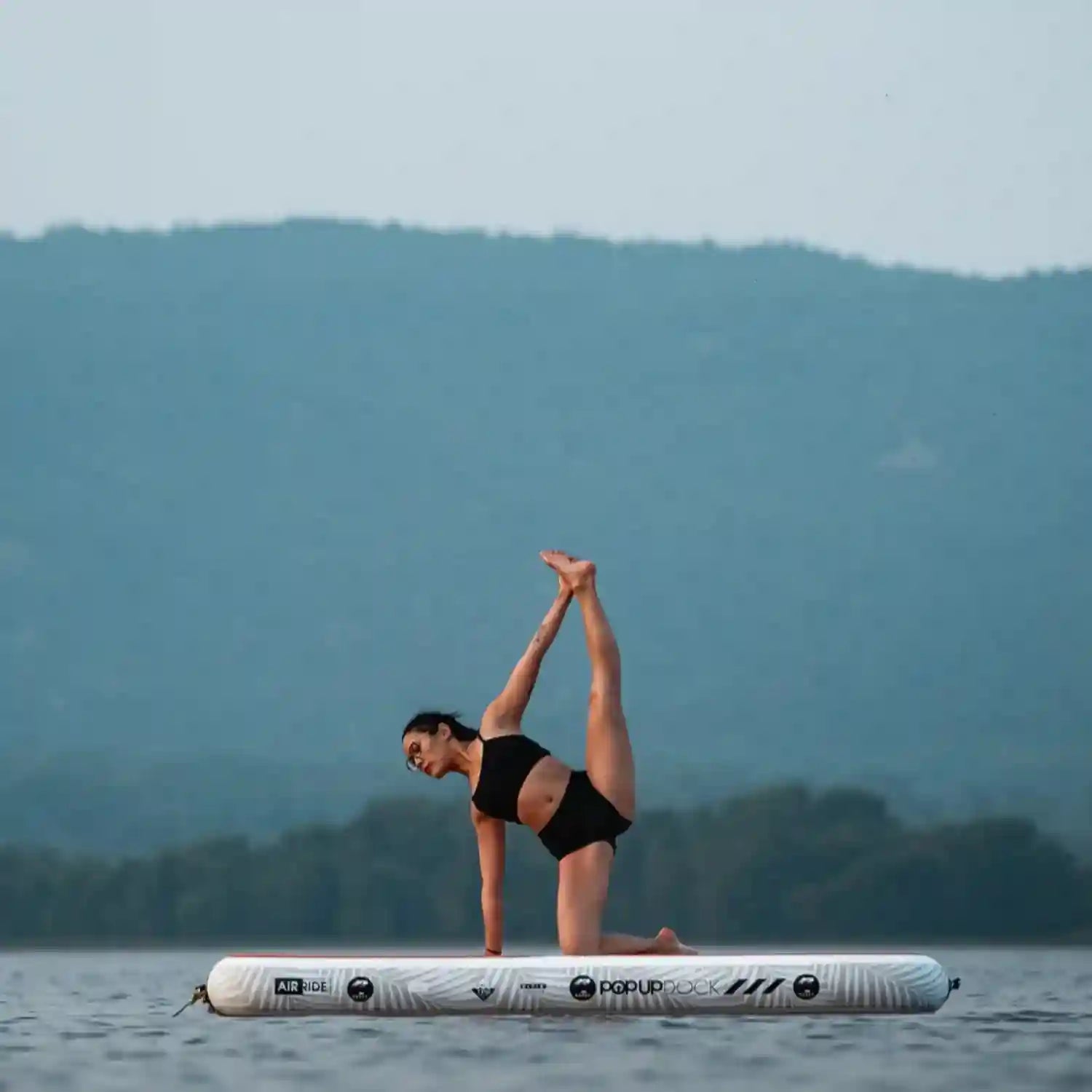 Woman performing yoga stretch pose on the POP inflatable dock, highlighting stability on water.