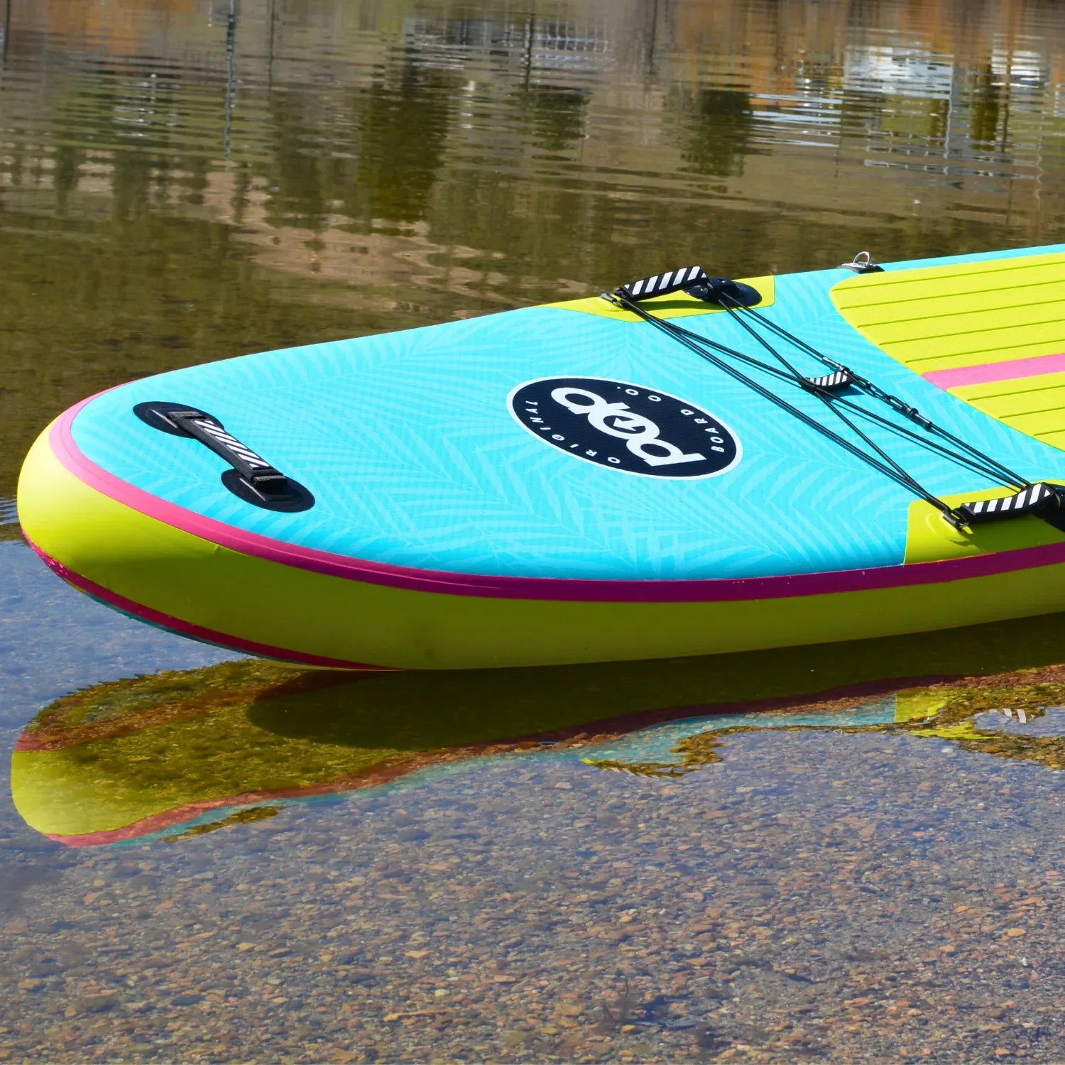 POP Yacht Hopper 11'0 inflatable paddleboard in turquoise, pink, and yellow resting on the shoreline.