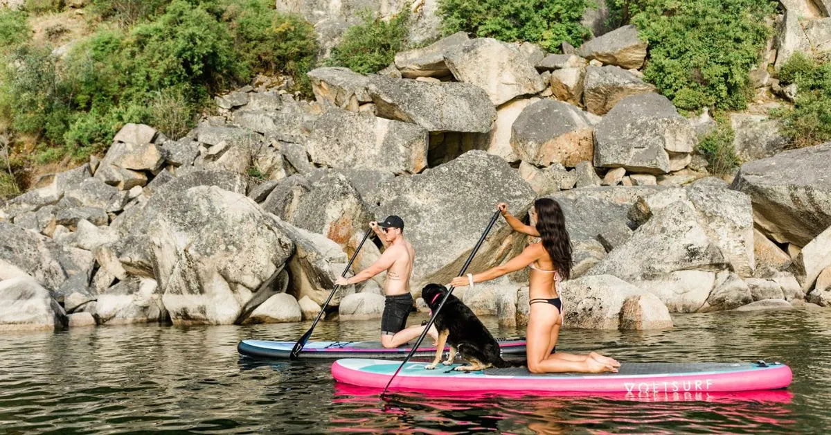 Couple paddleboarding with their dog on inflatable paddle boards on a calm Canadian lake