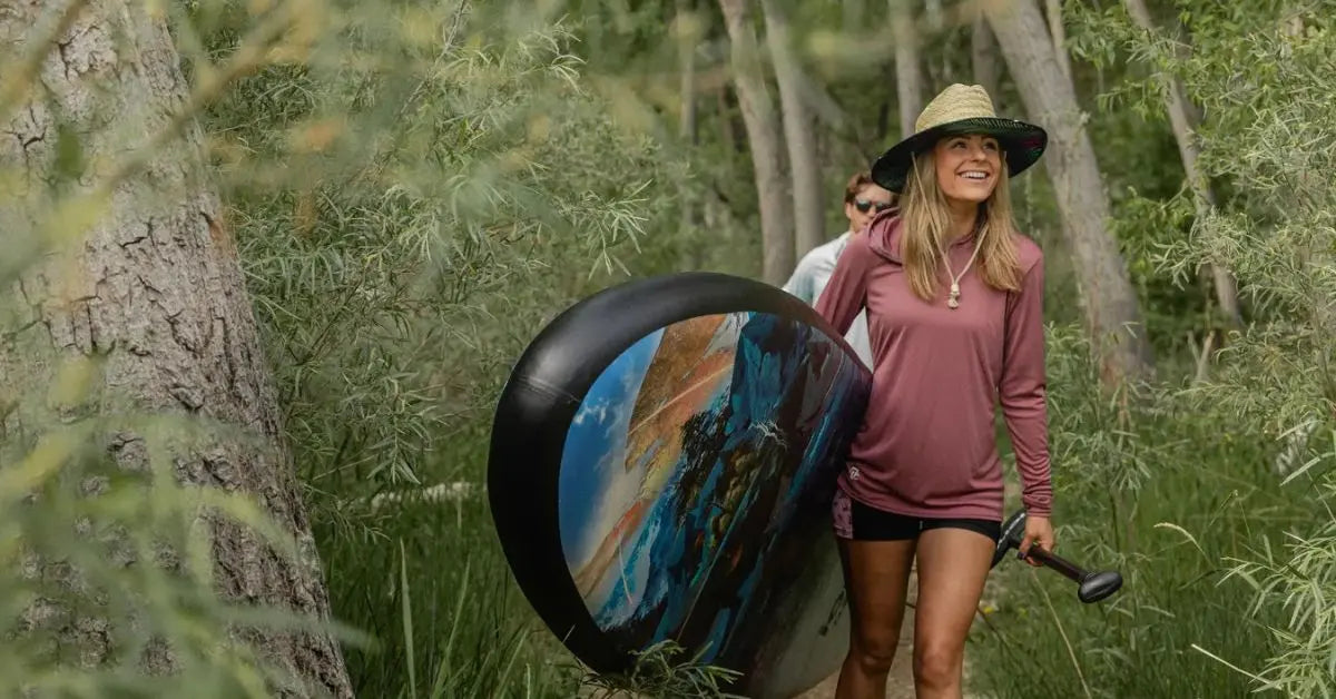 Woman carrying inflatable dock board through forest trail near waterfront