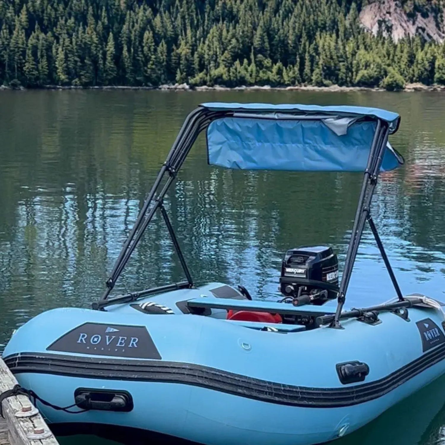Blue inflatable boat with canopy on a calm lake with trees in the background