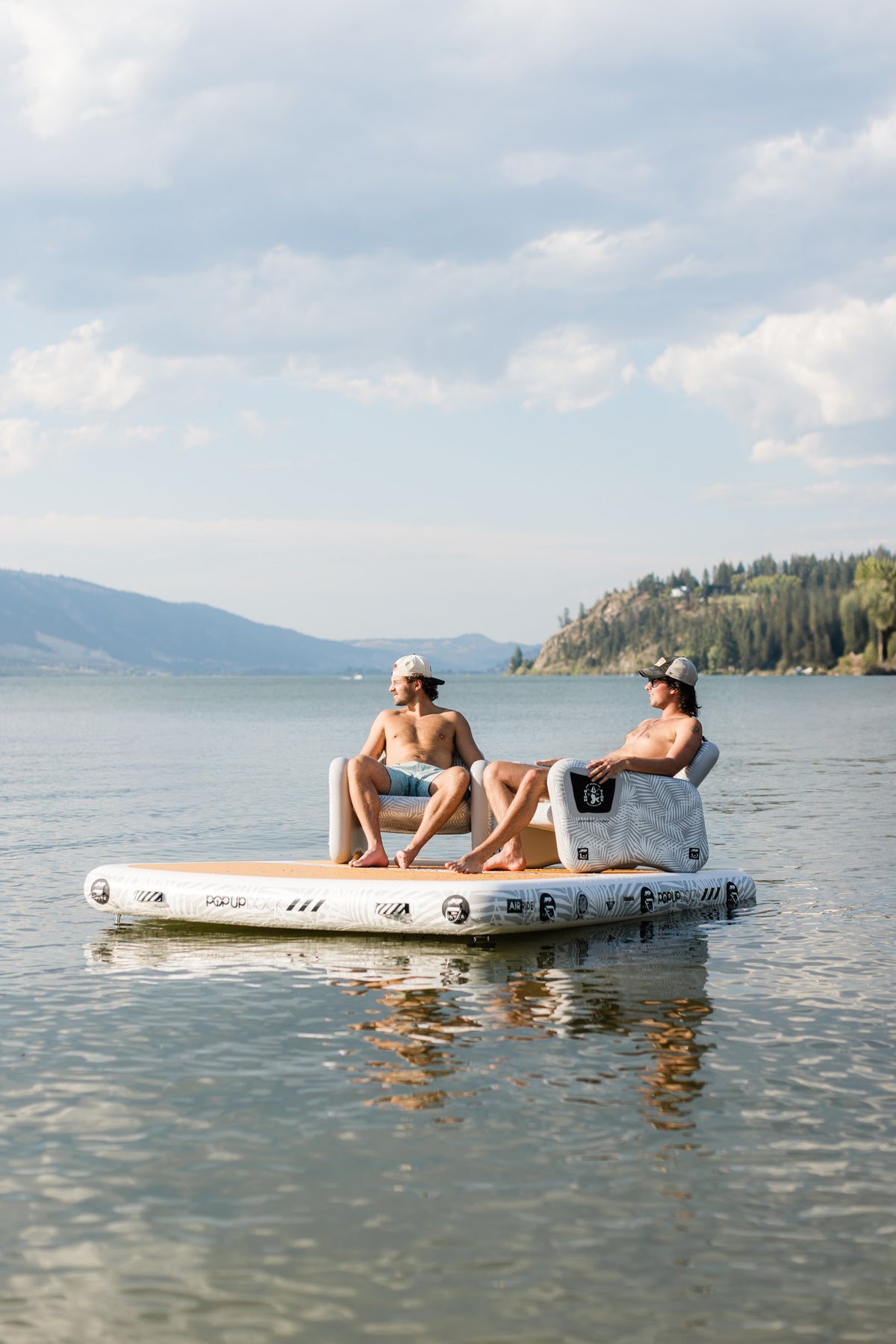 Two friends relaxing in POP Up chairs on an inflatable dock on Okanagan Lake, with a Canadian flag flying behind