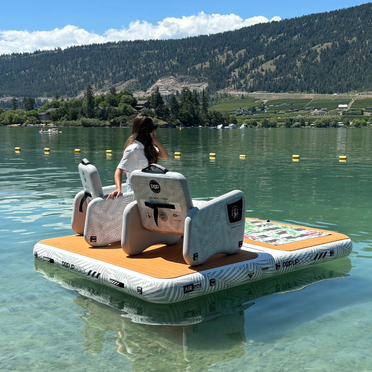 Back view of a woman lounging on the POP Dock and Chair Bundle floating on a calm lake.