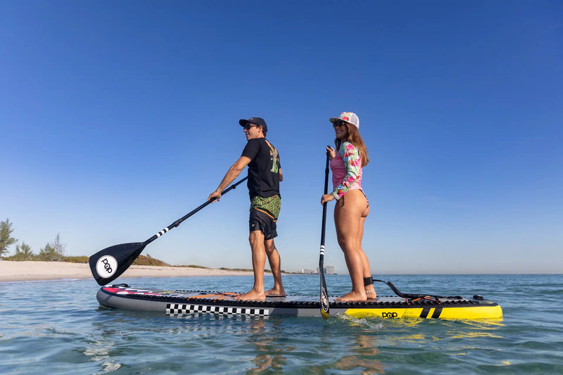 Two people paddleboarding on a clear day with a blue sky.