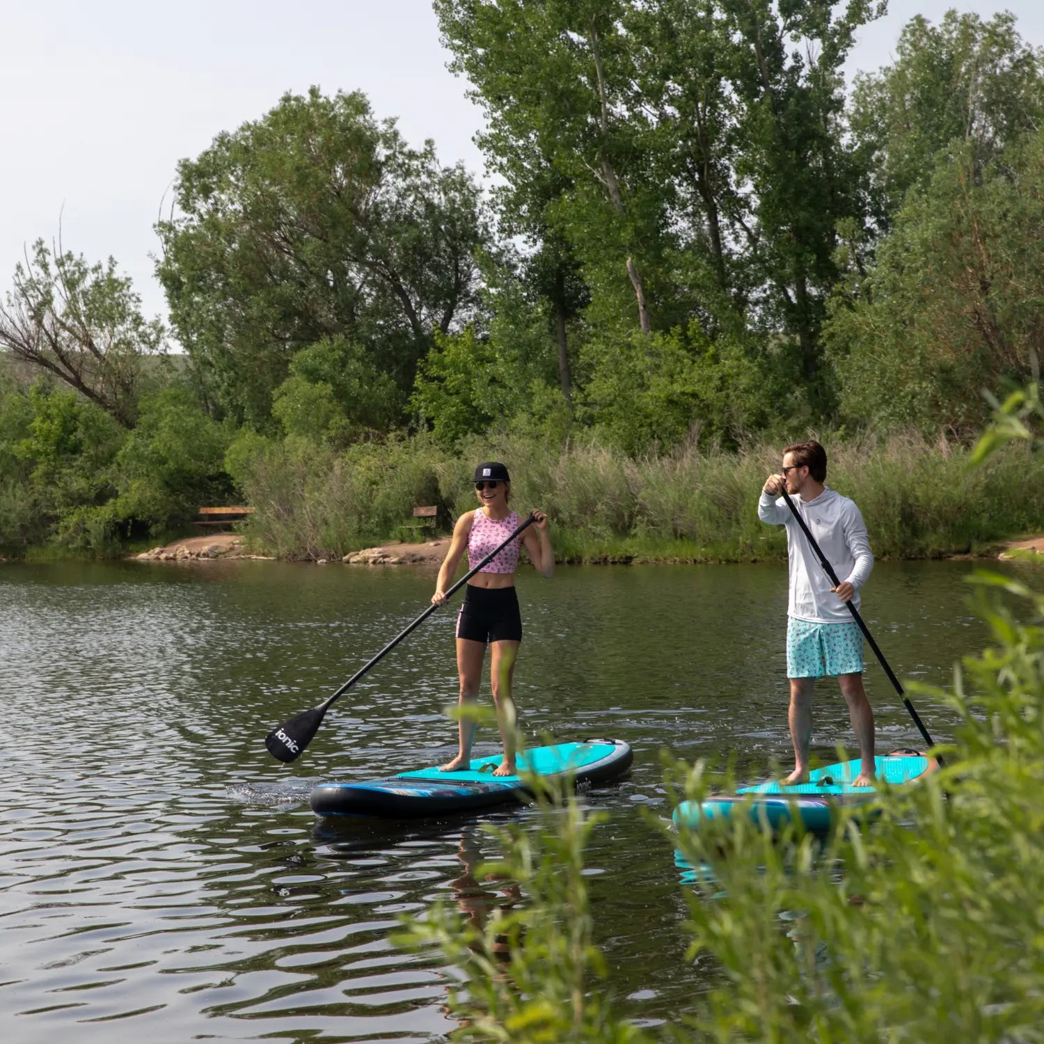 Man and woman paddling on Ionic Travis Parr paddle boards on calm lake.