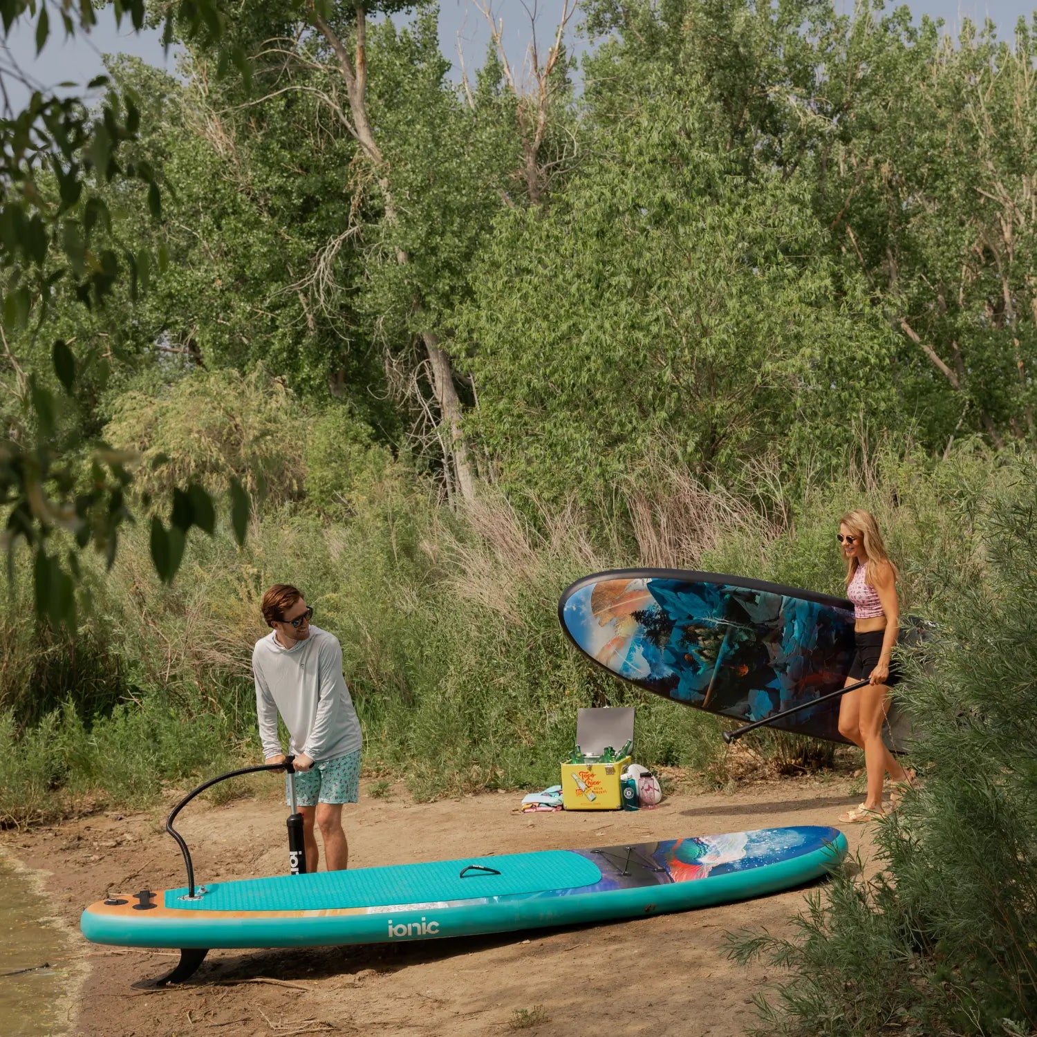 Man inflating Ionic paddle board while woman carries another Travis Parr edition SUP.