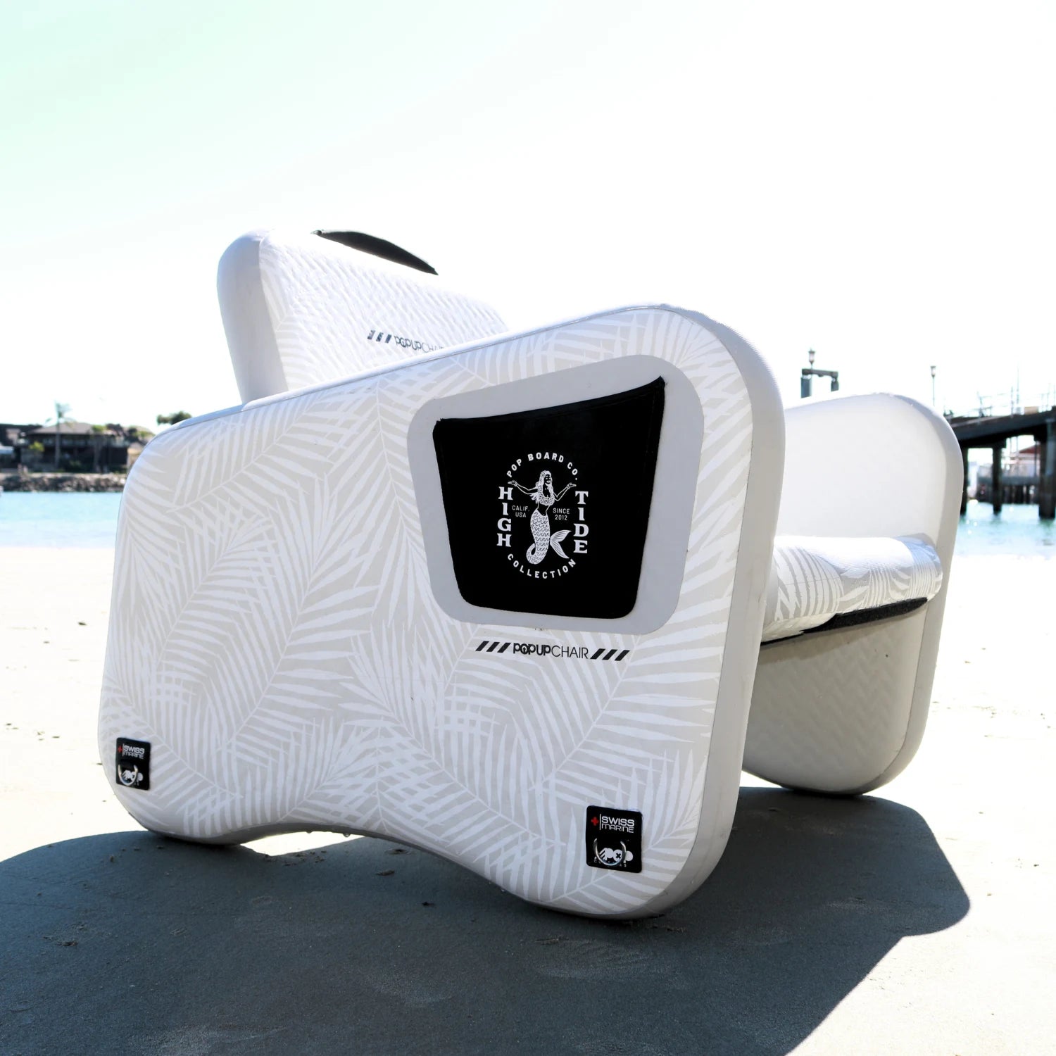 Angled view of POP Up Chair inflatable seat on beach, showing High Tide branding and premium PVC material.