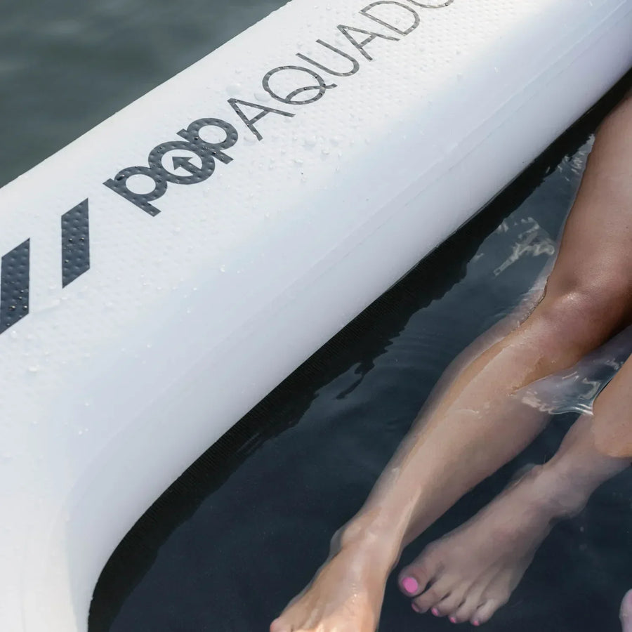 Close-up of the POP Aquadock inflatable platform showing the durable nylon net section where a person’s legs are resting in the water.