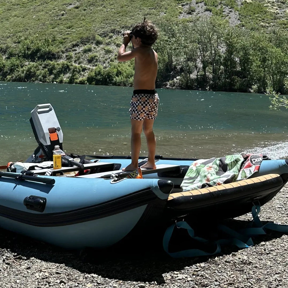Person standing on an inflatable boat by a lake with trees in the background