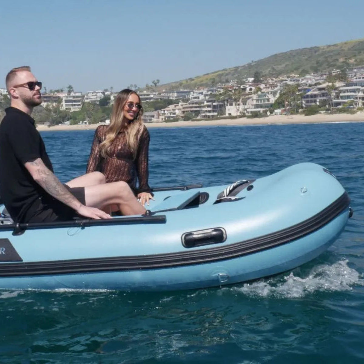 Two people on a blue inflatable boat with a coastal background