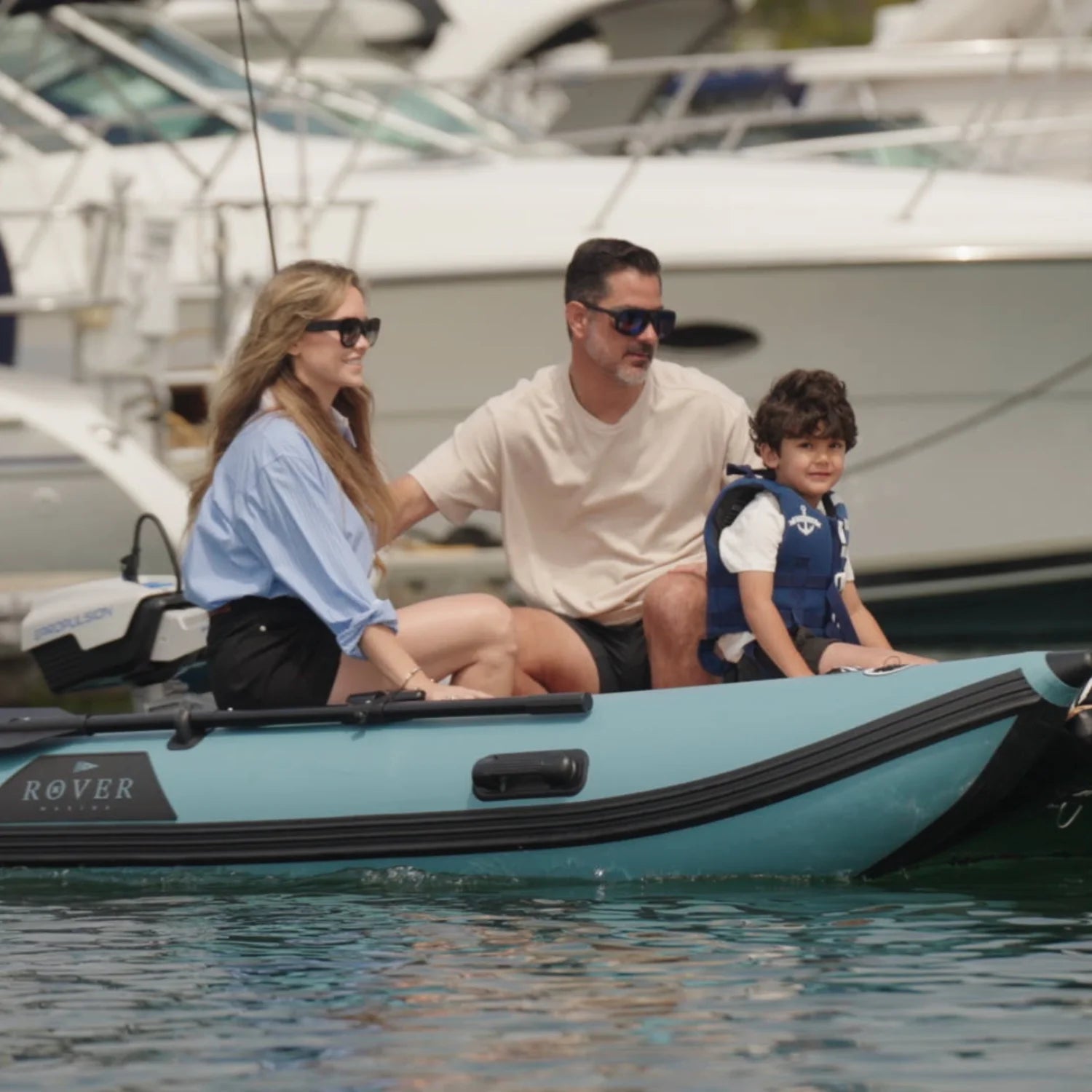 Family sitting together on Rover Marine Battle Cat inflatable boat surrounded by yachts.