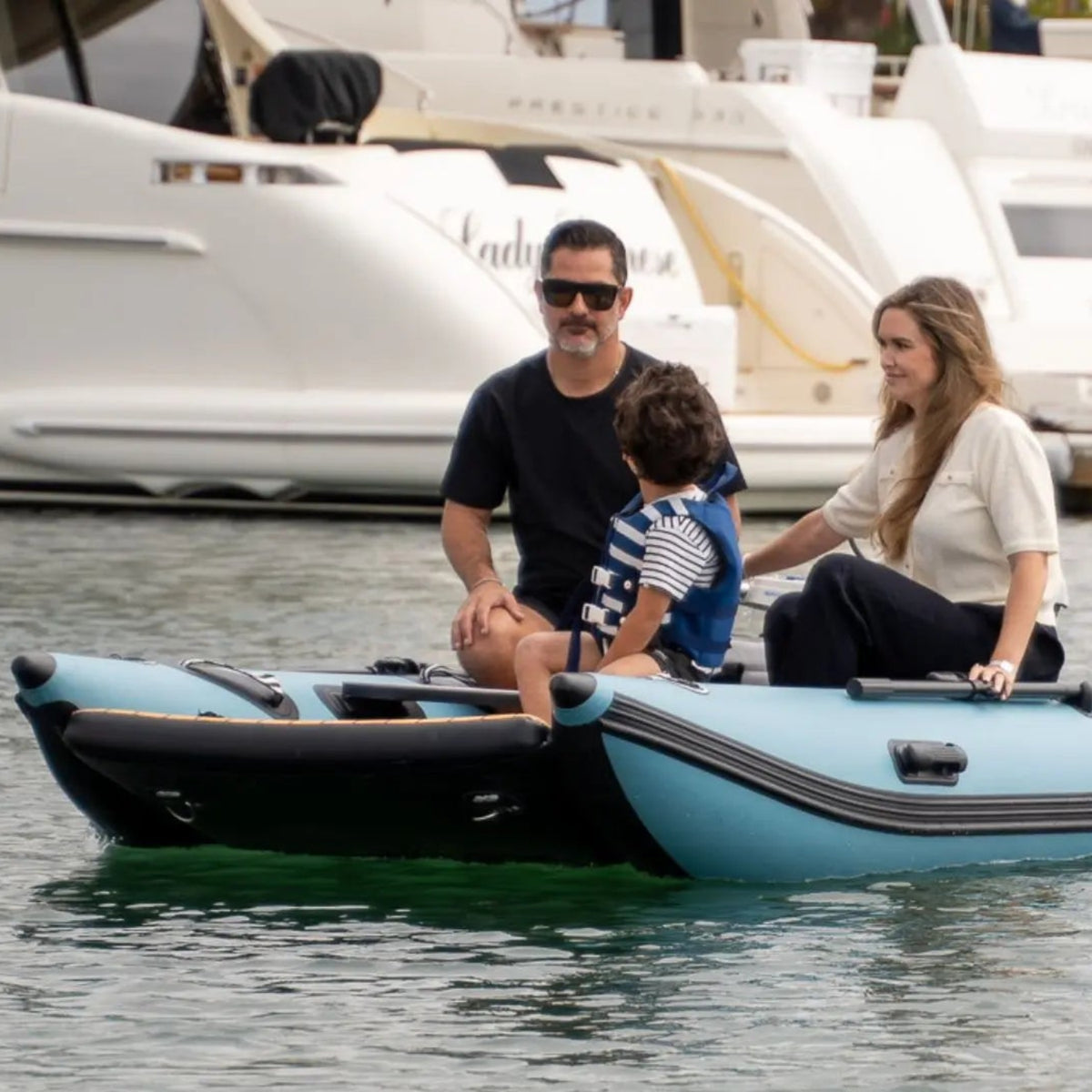 Family on a small inflatable boat in a marina with yachts in the background