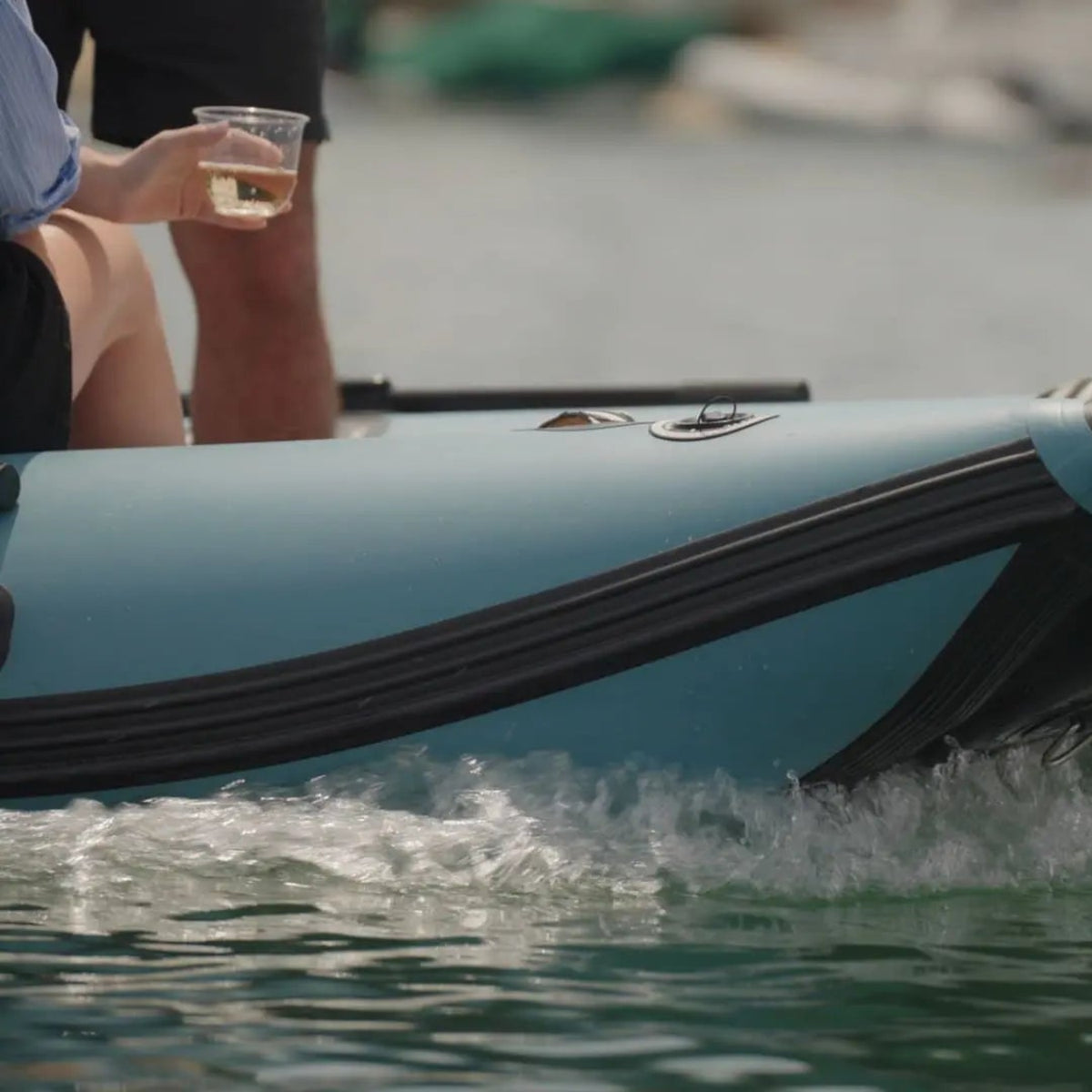 Inflatable boat speeding on water with a person holding a drink in the background