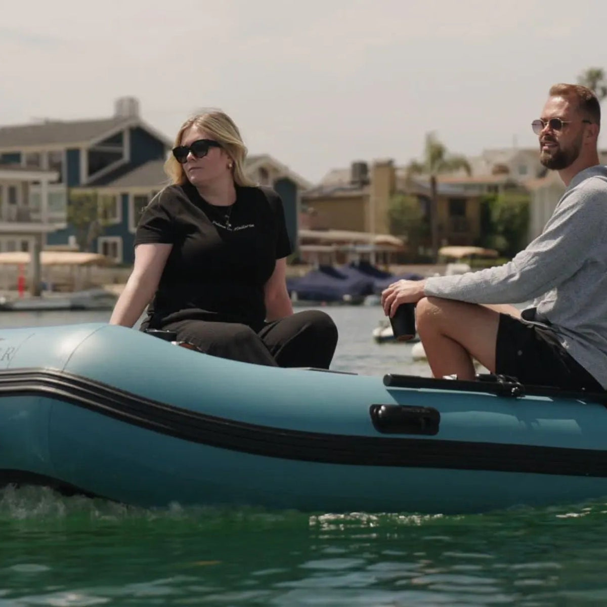 Two people on a blue inflatable boat in a harbor.