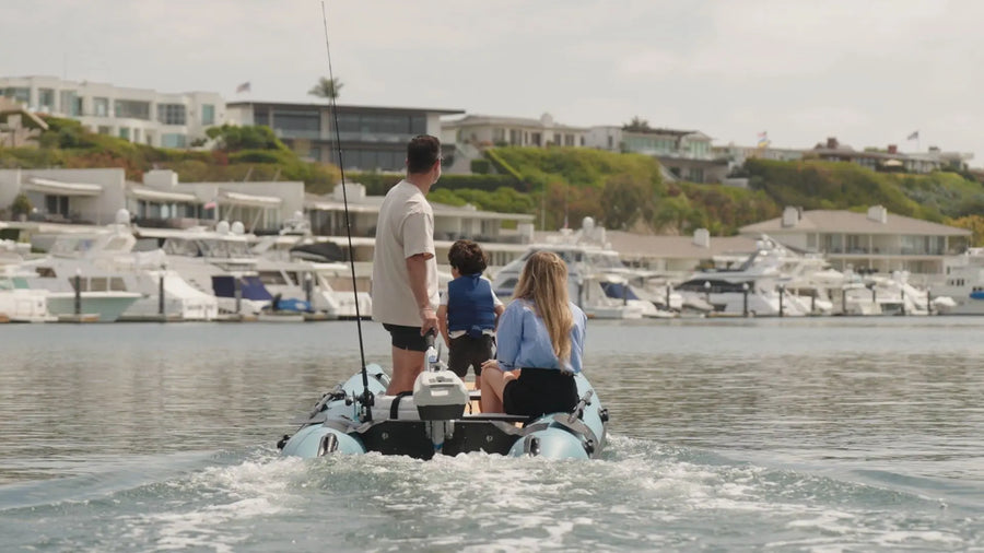 Two people on a small boat in a marina with houses and boats in the background.