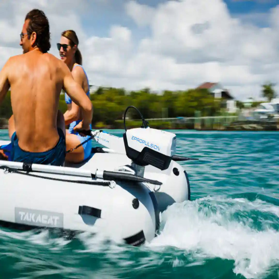 Two people on a electric outboard inflatable boat in the water with a scenic background.