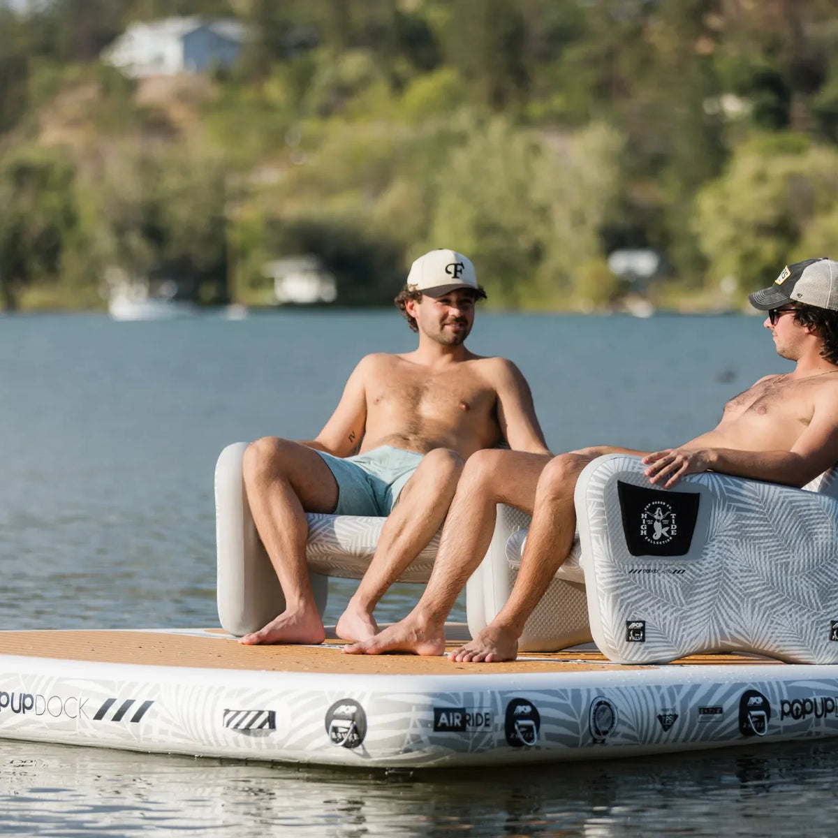 Two men relaxing shirtless on inflatable chairs placed on a floating dock, enjoying a sunny day by the water.